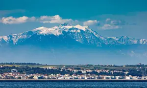 Majestatyczny góra Olimp, pokryta śniegiem, góruje nad nadmorskim miasteczkiem.