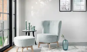 En bekväm fåtölj i turkos nyans, med en matchande pall och en blå vas med blommor.