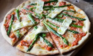 Pyszna pizza ze szparagami i serem brie, polana sosem pomidorowym, pokrojona na kawałki.