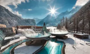 Zimowy relaks w **Dolinie Gastein**. Baseny termalne otoczone ośnieżonymi górami i lasem, z parą unoszącą się nad wodą.