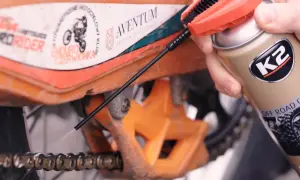 Ręka trzymająca puszkę smaru K2 i aplikująca go na łańcuch motocykla.