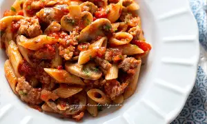 Piatto di pasta alla boscaiola con penne, funghi, salsiccia e pomodoro, un classico saporito.