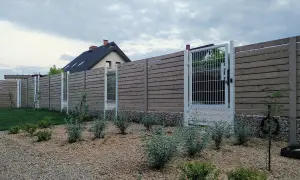 Nowoczesne ogrodzenie z drewnianych desek i metalowych słupków, z furtką. Czy ogrodzenie jest obiektem budowlanym? W tle dom.