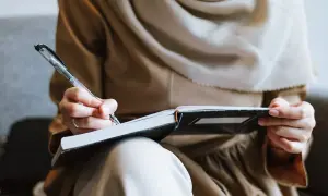 Kobieta w hidżabie pisze w notatniku, przygotowując się do rozmowy z potencjalnym pracodawcą.