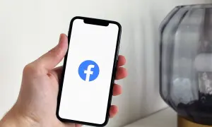 Dłoń trzyma smartfon z logo Facebooka. Chcesz wiedzieć, jak wyłączyć widoczność na FB?