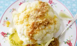 Ganzes Blumenkohlröschen mit Butter und Bröseln beträufelt, serviert auf einem Teller mit Blumenmuster. Tolle Idee für Blumenkohl Rezepte!