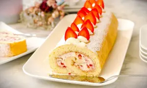 Eine köstliche Biskuitrolle mit Erdbeerfüllung, verziert mit frischen Erdbeeren und Sahnetupfern. Ein Klassiker, der an Omas Biskuitrolle Landfrauen erinnert.