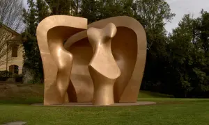 Escultura abstracta dorada en el parque de los pueblos de Europa, con formas curvas y orgánicas, rodeada de césped y árboles frondosos.