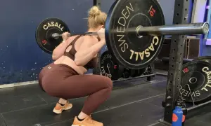 En kvinna gör squats svenska med en skivstång på axlarna i ett gym.