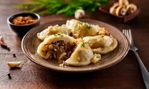 Talerz pełen pysznych, domowych pierogów z kapustą i grzybami, posypanych szczypiorkiem. Obok czosnek i pieprz.
