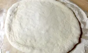 Pâte à pizza étalée sur une surface farinée, prête pour une recette pâte à pizza rapide.