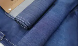 Niebieski poliester w jeansach, zwinięty w rolki, z widocznymi białymi szwami i metką.