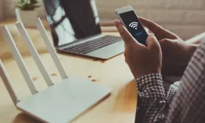 Dłoń trzyma smartfon z ikoną Wi-Fi i przyciskiem "connect", obok router i laptop. Szybkie połączenie dzięki wifi direct.