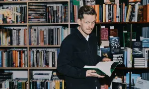 Robin Olovsson står bland bokhyllor och håller en öppen bok.