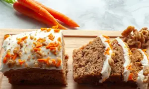 Saftiger karottenkuchen mit cremigem frosting, garniert mit geriebenen Karotten und Walnüssen. Daneben liegen frische Karotten und Nüsse.