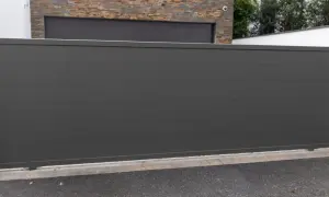 Szara brama przesuwna z poziomymi przetłoczeniami, przed budynkiem z kamienną okładziną.