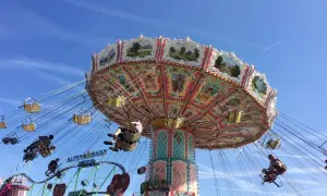 Carrusel giratorio en un oktoberfest parque de atracciones, con gente disfrutando del paseo bajo un cielo azul.