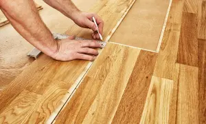 Un bricoleur utilise une règle et un crayon pour marquer une ligne de coupe sur du parquet flottant, étape essentielle pour savoir comment couper du parquet flottant.