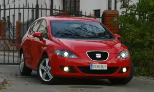 Czerwony Seat Leon 2 z włączonymi światłami, zaparkowany przed bramą.