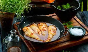 Kycklingvingar i en glansig, kryddig egen marinad i en stekpanna, redo för grillen. Bredvid finns färska örter och flingsalt.