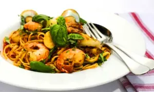 En tallrik med linguine frutti di mare, toppad med färska örter och serverad med bestick.