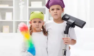 Dzieci z odkurzaczem i miotełką do kurzu, z minami sugerującymi, że obowiązki dziecka to nie zabawa.