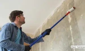 Mann mit Schutzbrille trägt eine Grundierung auf eine rohe Wand auf, um sie für die weitere Bearbeitung vorzubereiten.