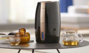 Elegancki nawilżacz ewaporacyjny Philips, obok szklanej filiżanki z herbatą i ozdobnej buteleczki. Czy do nawilżacza ewaporacyjnego można dodać olejek?