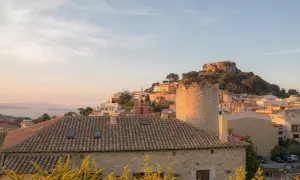 Sonnenuntergang über einem Dorf an der Girona Costa Brava. Ein alter Turm und ein Schloss auf einem Hügel über weiß getünchten Häusern.