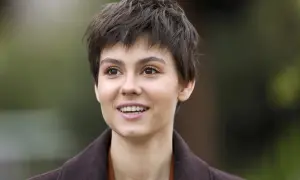 Uśmiechnięta Pola Gonciarz, w brązowym płaszczu, wygląda jakby właśnie usłyszała coś zabawnego od swojego partnera.