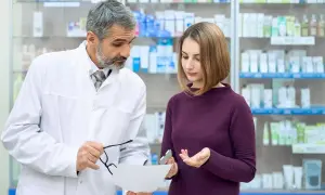 Doświadczony farmaceuta doradza klientce w aptece, wskazując na receptę i opakowanie leku.