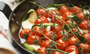 Saftige cherry tomaten mit Knoblauch und Lorbeerblättern in einer Pfanne, bereit zum Garen.