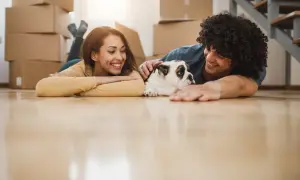 A happy couple and their bulldog relax on the floor amidst moving boxes, ready for their new home.