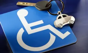 Chiave e portachiavi a forma di auto su un cartello blu con simbolo di disabilità, evocano la necessità di un fac simile certificato medico per IVA agevolata.