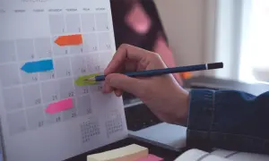 Kalender med färgglada post-it-lappar markerar viktiga datum. En hand med en penna planerar för bokslut enskild firma.