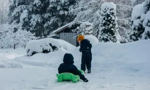 Dzieci cieszą się feriami zimowymi w Małopolsce, zjeżdżając na sankach po ośnieżonym podwórku.