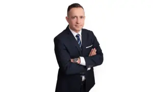 Mężczyzna w garniturze ze skrzyżowanymi rękami, na białym tle.