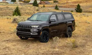 Ciemny Jeep Grand Wagoneer na tle wiejskiego krajobrazu z budynkami i drzewami.