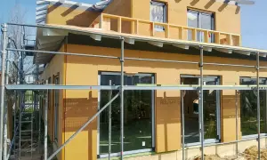 Casa en construcción con paredes exteriores prefabricadas de madera, andamios y cielo azul.