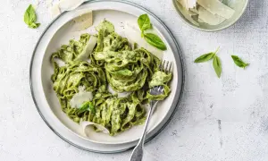 Un piatto di pasta al pesto, condita con una cremosa salsa verde, guarnita con scaglie di parmigiano e foglie di basilico fresco.
