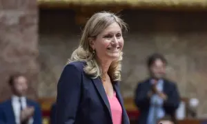 Une femme souriante, peut-être Vianney Pivet, d'origine inconnue, porte un blazer rayé et un haut rose.