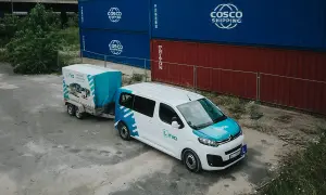 Biały bus z przyczepą, na tle kontenerów. Zastanawiasz się nad prawem jazdy B+E koszt? To idealny zestaw do nauki.