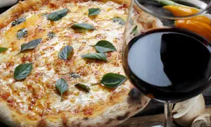 Pizza fumante con basilico e un bicchiere di vino rosso, il perfetto vino per pizza.
