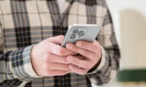 Osoba w kratę trzyma smartfon, szukając informacji, jak odzyskać usunięte wiadomości SMS.