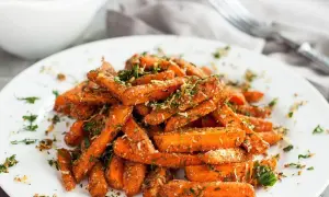 Karmelizowana marchewka, posypana ziołami i parmezanem, podana na białym talerzu.