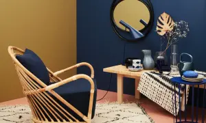 Ein Rattansessel mit dunkelblauem Kissen steht auf einem flauschigen Teppich. Daneben ein Tisch mit Deko. Welche Farbe passt zu Gold? Dunkelblau und Senfgelb harmonieren perfekt.