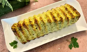 Un délicieux pain de courgettes, doré et savoureux, servi sur une assiette blanche. Parfait pour un repas léger.