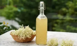 Kwiat bzu czarnego syrop w butelce z korkiem i koszyku pełnym kwiatów.