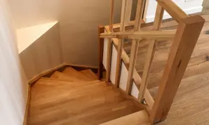 Holztreppe mit geschwungenen Stufen und einem hölzernen Geländer. Die Treppenstufen streichen das Licht und laden zum Hinaufgehen ein.