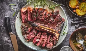 Aufgeschnittenes, perfekt gegrilltes Bistecca alla Fiorentina mit Rosmarin und Beilagen.